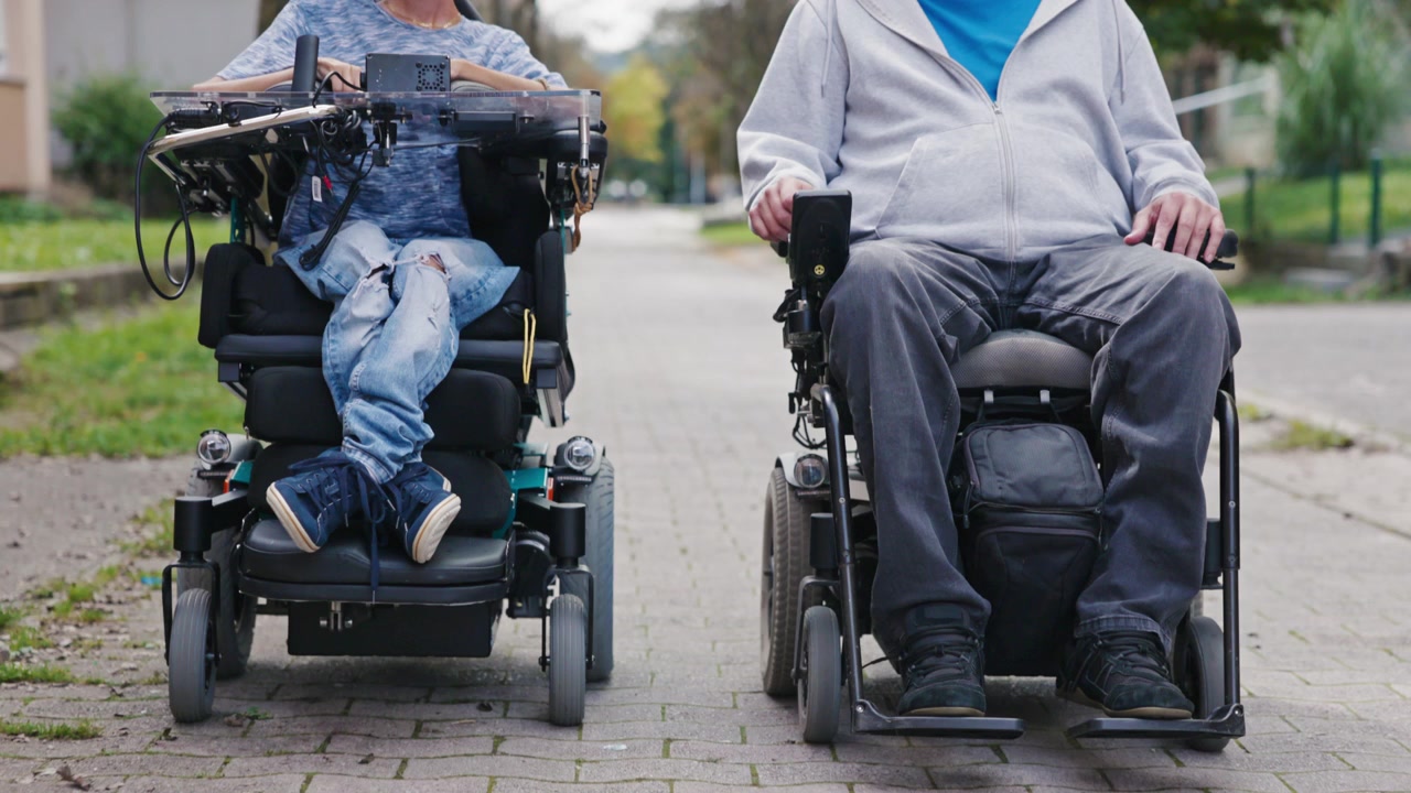 Two men using powered wheelchairs navigating an accessible city walkway enjoying independent