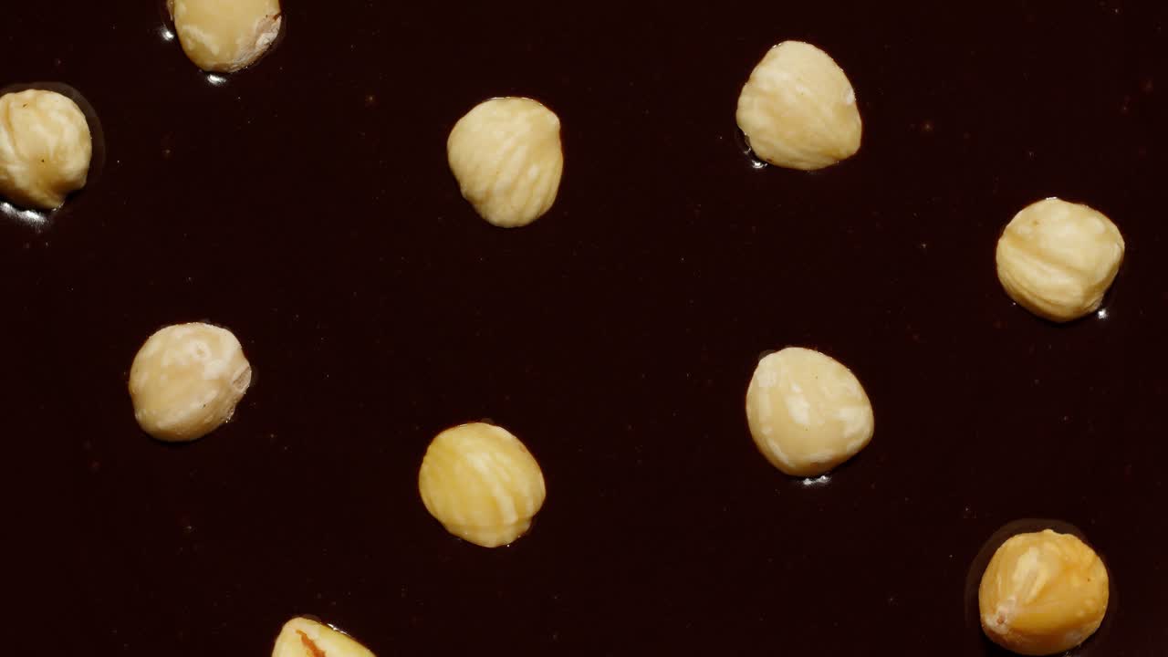 Melted liquid dark chocolate and hazelnuts rotating close-up top view of molten liquid hot chocolate