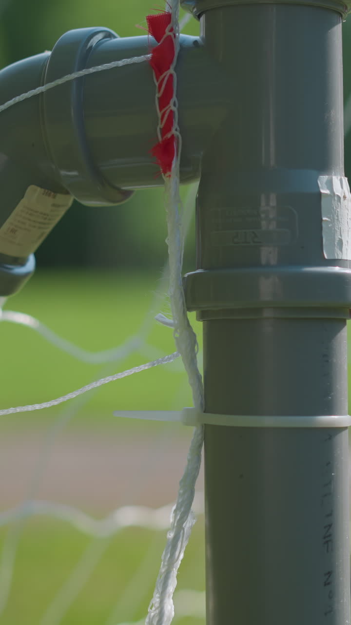 축구 골포스트의 클로즈업으로 공이 이미 네트에 렸으며, 골키퍼가 공이 들어간 후 공을 가져오기 위해 손을 는 흐릿한 시각을 보여줍니다.