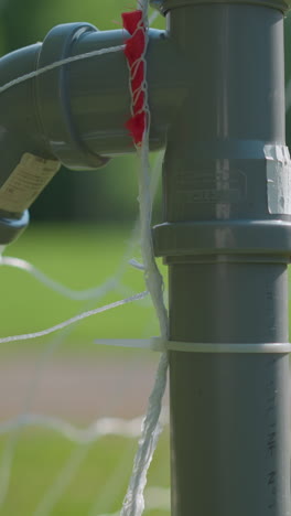 close-up of a soccer goalpost with a ball already shot into the net, showing a blurred view of the goalkeeper reaching to retrieve the ball after it has entered