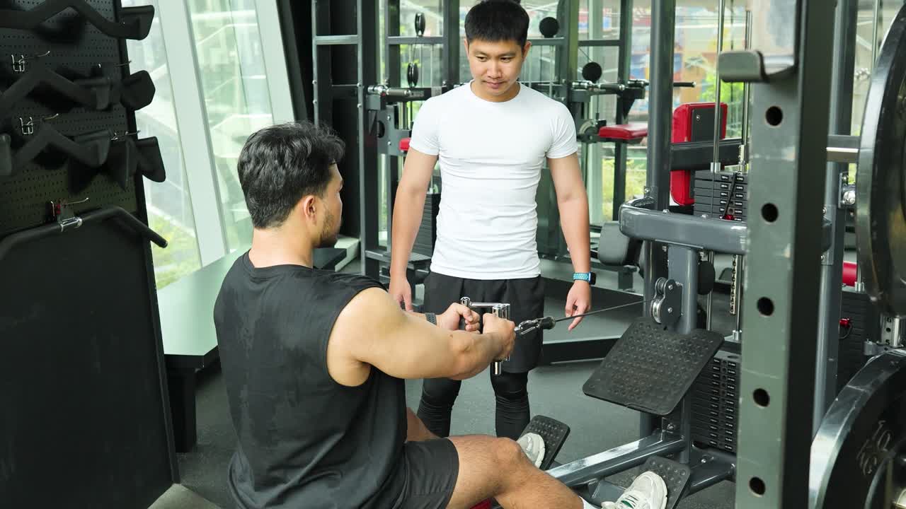 Two men exercise using a cable machine in a well-lit gym, focusing on strength training and teamwork