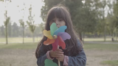 cute latin girl playing with paper fan and blowing on it in the park