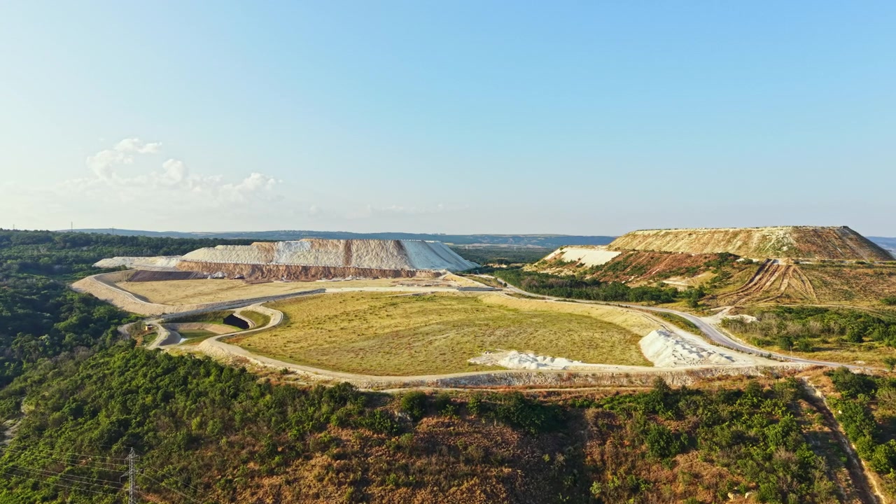 Landscape showing mining site with large piles of earth and machinery located in open area during sunny day