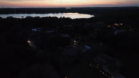 dark neighborhood in florida and lake during golden sunset at horizon. aerial top down flyover. cars on main street. dark residential area in plant city, florida