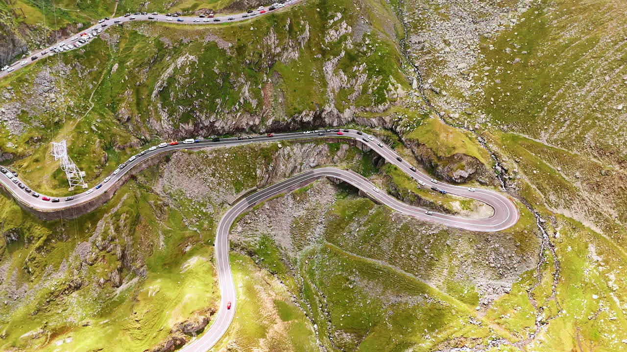 Winding mountain road scenery. Cars navigate a winding road surrounded by lush green mountains and rocky terrain under clear skies