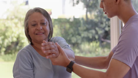 assisting with arm stretching exercise, physiotherapist helping senior woman indoors