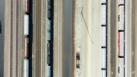 bird's-eye-view-truck-forward-drone-shot-flying-over-railroad-station-in-a-desert-environment-on-a-sunny-day-with-cargo-and-tank-tain-and-powerlines