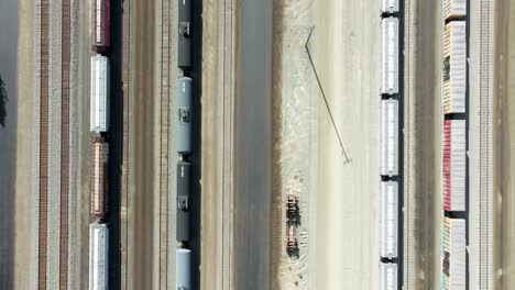 Drohne-Aus-Der-Vogelperspektive,-Die-An-Einem-Sonnigen-Tag-Mit-Fracht--Und-Tanktank-Und-Stromleitungen-über-Dem-Bahnhof-In-Einer-Wüstenumgebung-Fliegt