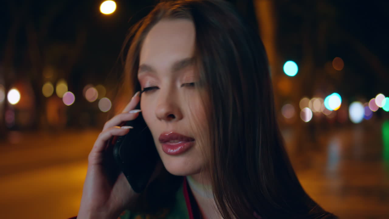 아름다운 여자가 스마트폰으로 이야기하고 있습니다. 밤에 마을을 가게 지켜보고 있습니다. 여성이 전화하고 있습니다.