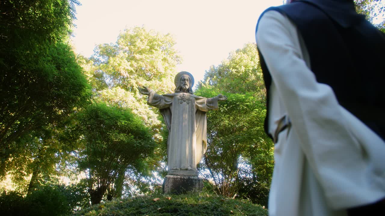 increíble disparo de cardán en una escena con un monje rezando en una estatua de jesús en el bosque