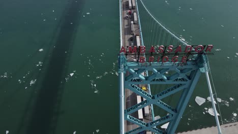 logo of ambassador bridge with many semi trucks pilling on bridge, aerial view