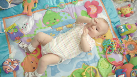 Little-baby-lying-back-on-colorful-carpet-with-toys.-Infant-boy-portrait