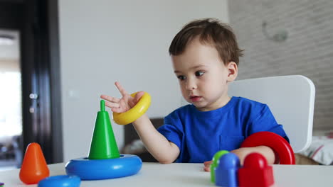 baby boy put the rings from toy pyramid on his hands. lovely child assembles the toy.