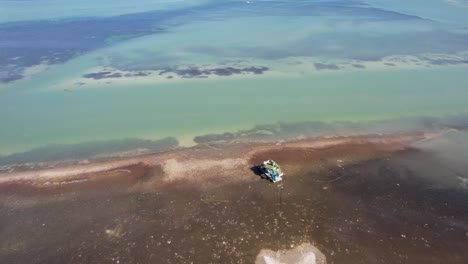 Drone-clip-over-beachside-forest-with-playground-on-the-shoreline,-then-moving-over-clear-sea-water-and-reef-structure-with-seaweed