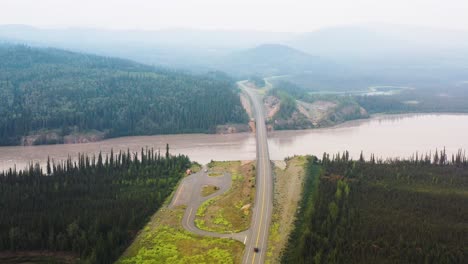 aerial drone shot flying high over a bridge surrounded by dense coniferous forest with the view of a camping site close beside alaskan highway in usa at daytime