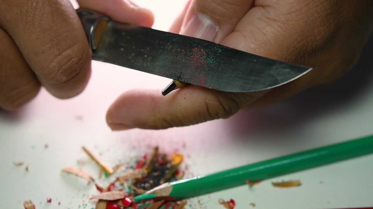 Opptak av hender som sakte spisser en blyant og noen fargeblyanter med en skarp kniv
