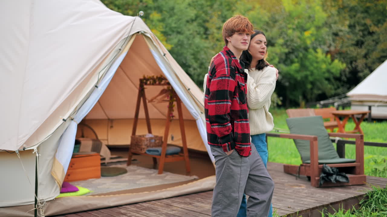 Una coppia che si abbraccia e parla sulla terrazza di una tenda in un glamping. Rigogliosa foresta circostante