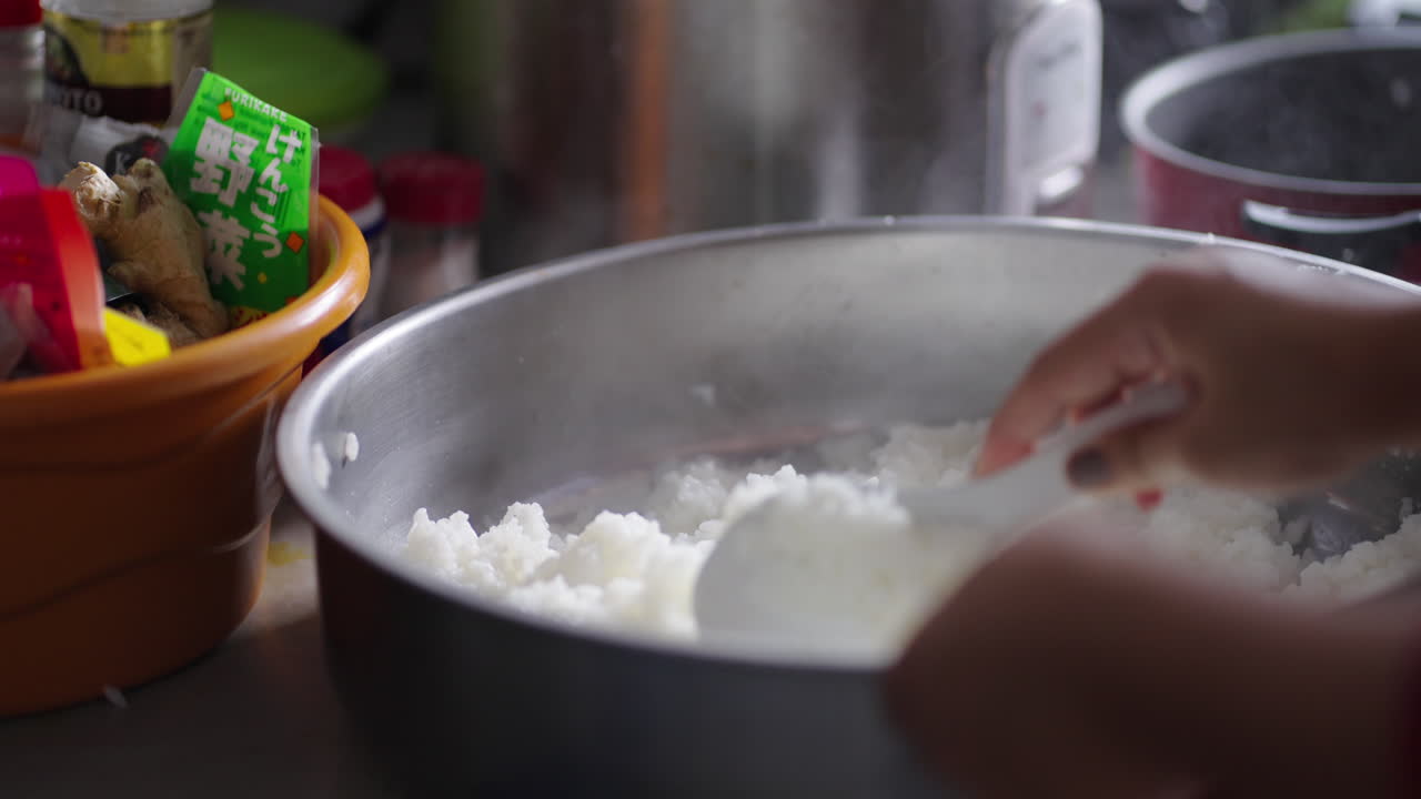 Close-up of hot, boiling sushi rice being stirred by hands to avoid burning during preparation