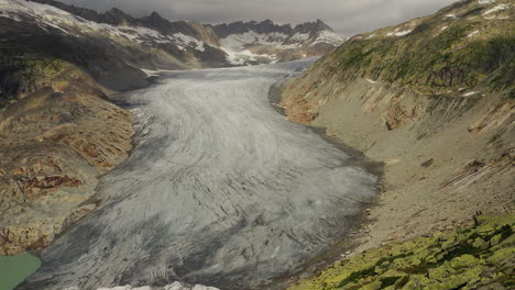 Drone-tilt-up-reveal-shot-of-Rhone-Glacier-during-cloudy,-summer-day