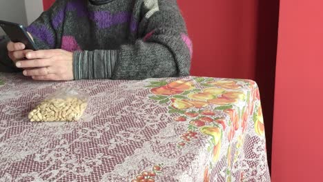 mujer blanca comiendo maní en una mesa y usando un teléfono celular