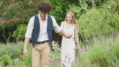 Happy-diverse-couple-walking-in-garden-on-sunny-day-at-wedding