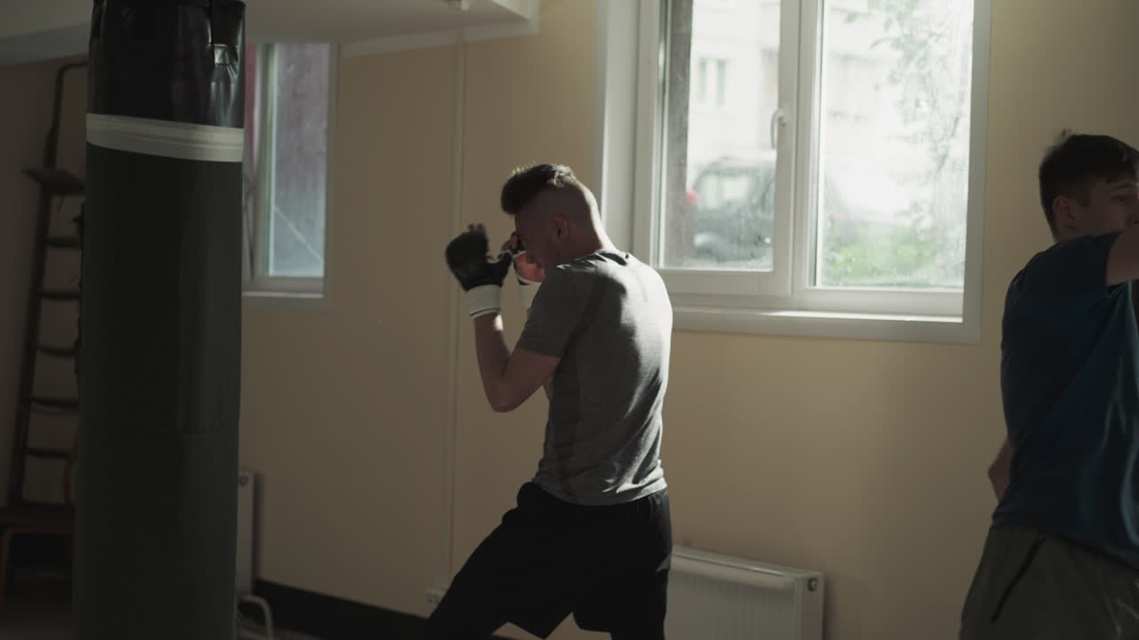 복싱에 종사하는 스포츠 의복을 입은 강한 운동선수 그룹은 복싱 봉투를 때립니다. 신체적 체력을 향상시키고 신체 근육을 구축합니다. 타격을 통해 부정적인 감정을 아 니다.