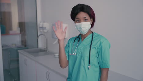 young female doctor with a facemask says hello to the camera