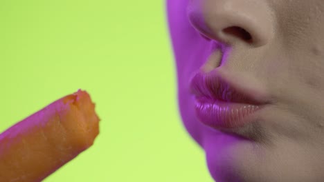 woman taking a bite from carrot in close-up, neon color background