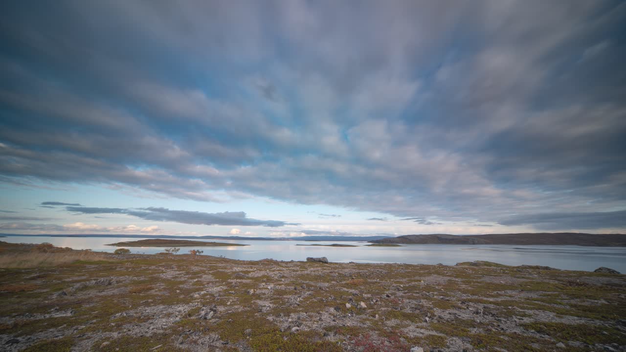 las nubes delgadas son llevadas por fuertes vientos sobre la costa rocosa de un fiordo con escasa vegetación en un video de time-lapse