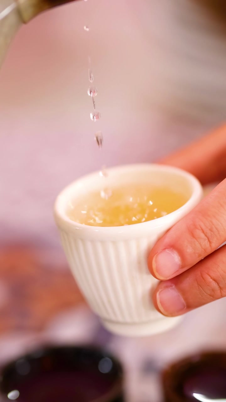 Una persona versa tè aromatico da una teiera a strisce in una tazzina, il tutto ripreso con illuminazione calda.