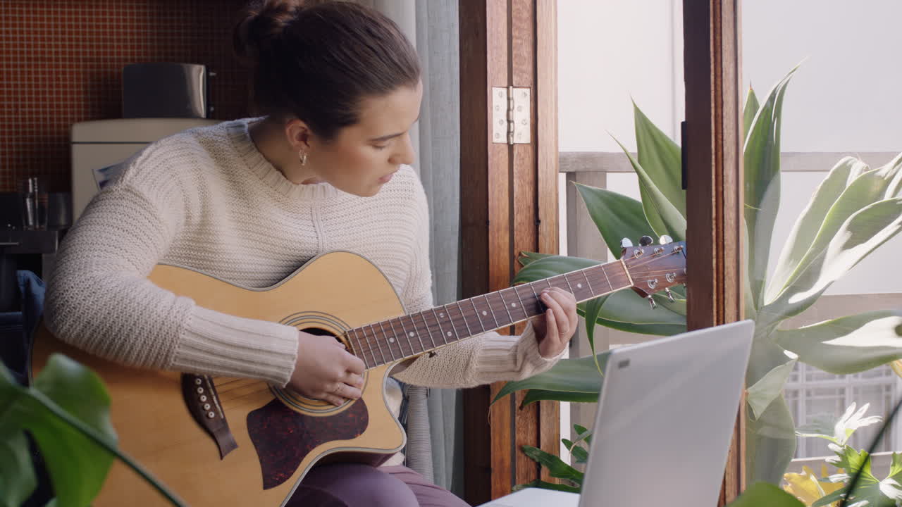 mujer joven tocando la guitarra en casa aspirante a músico aprendiendo a tocar un instrumento musical usando una computadora portátil disfrutando de la expresión creativa practicando música