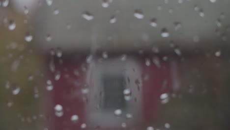 Rain-Drops-on-Window-To-Red-Old-House-In-Fall,-Handheld-Close-Up-Rack-Focus-To-Medium-Shot