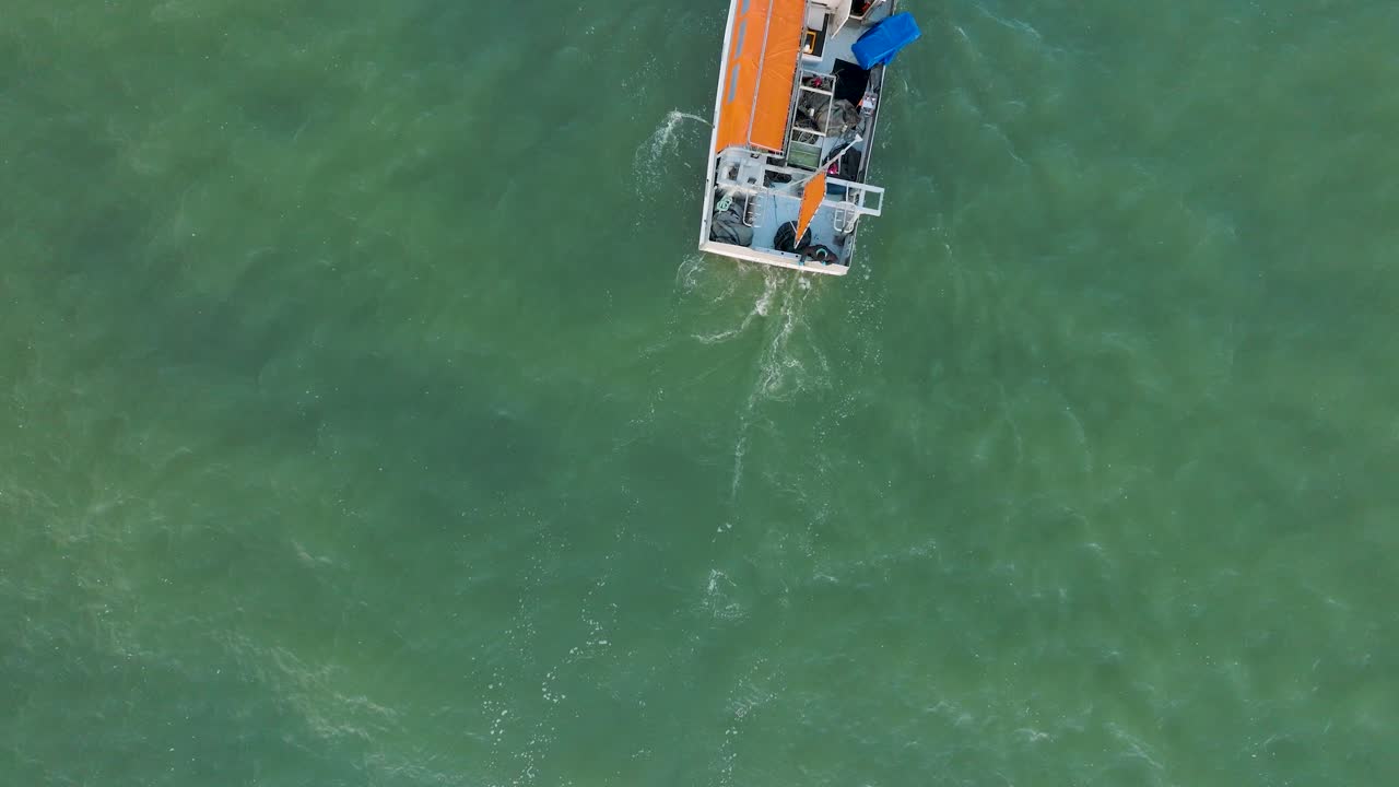Veduta aerea di un peschereccio costiero che naviga nel tranquillo Mar Baltico, un pescatore che cala la rete da pesca in acqua, giornata di sole, spiaggia di sabbia bianca distante, ampia ripresa aerea con drone in avanzamento.
