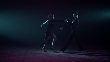 ballroom couple dancing on dark stage. dancers practicing latin dance indoors.