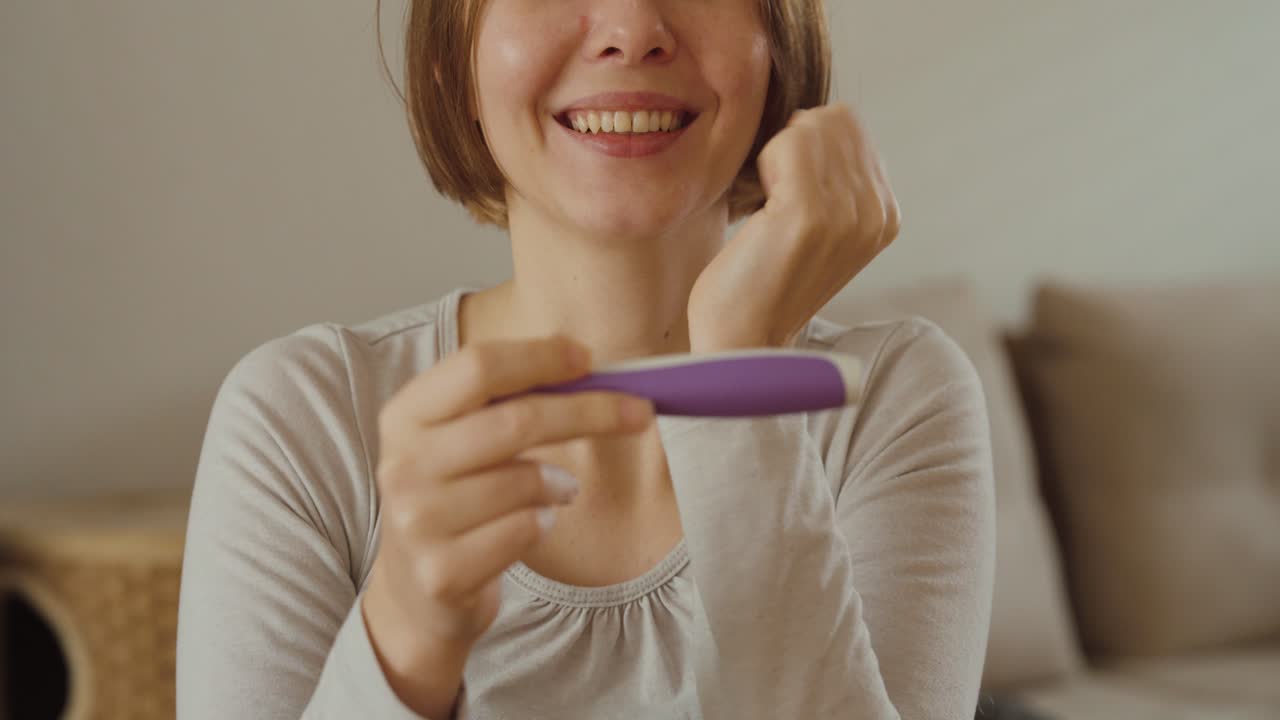 Una mujer alegre sonríe y celebra tras ver un resultado positivo en una prueba de embarazo: concepto de felicidad, nuevos comienzos y planificación familiar