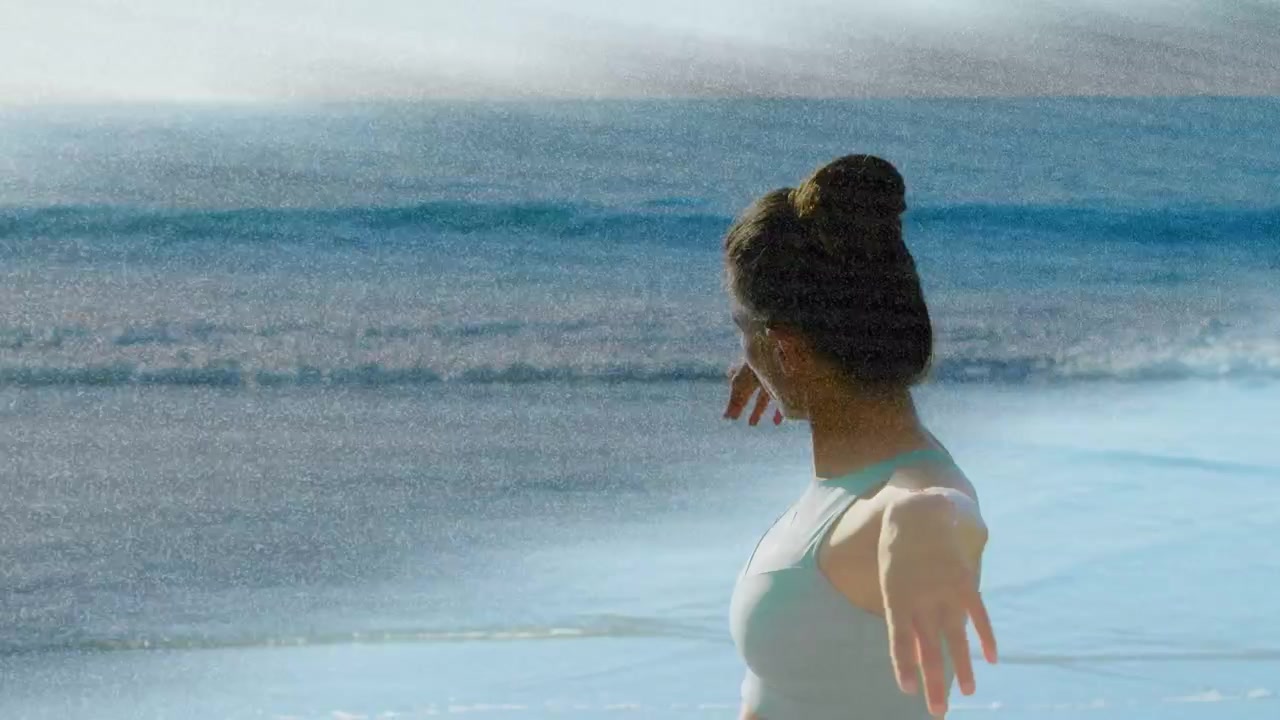 Woman holding bent arms and unfolding into flowing fitness stretch by ocean, light streaks passing