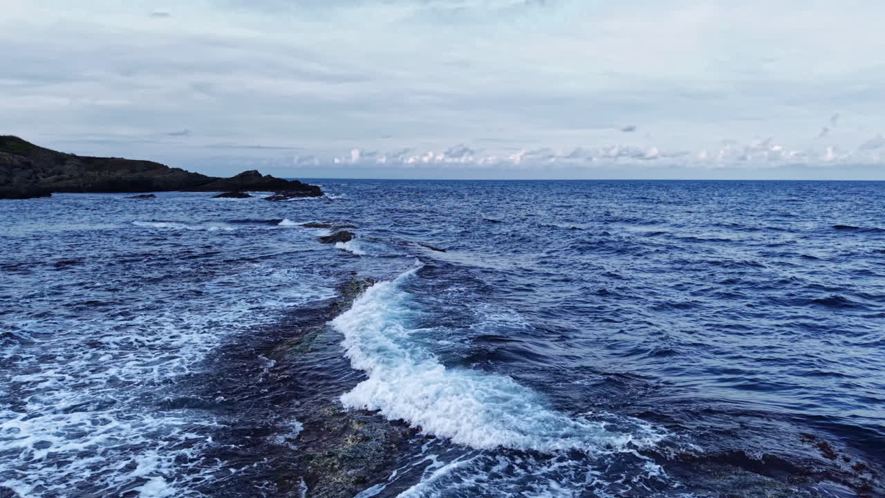Bølgene danser forsiktig langs den steinete strandlinjen mens skyene omfavner det rolige havet under en myk kveldshimmel