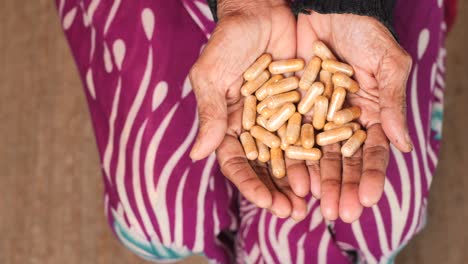 elderly woman's hands holding a pile of brown medicine capsules