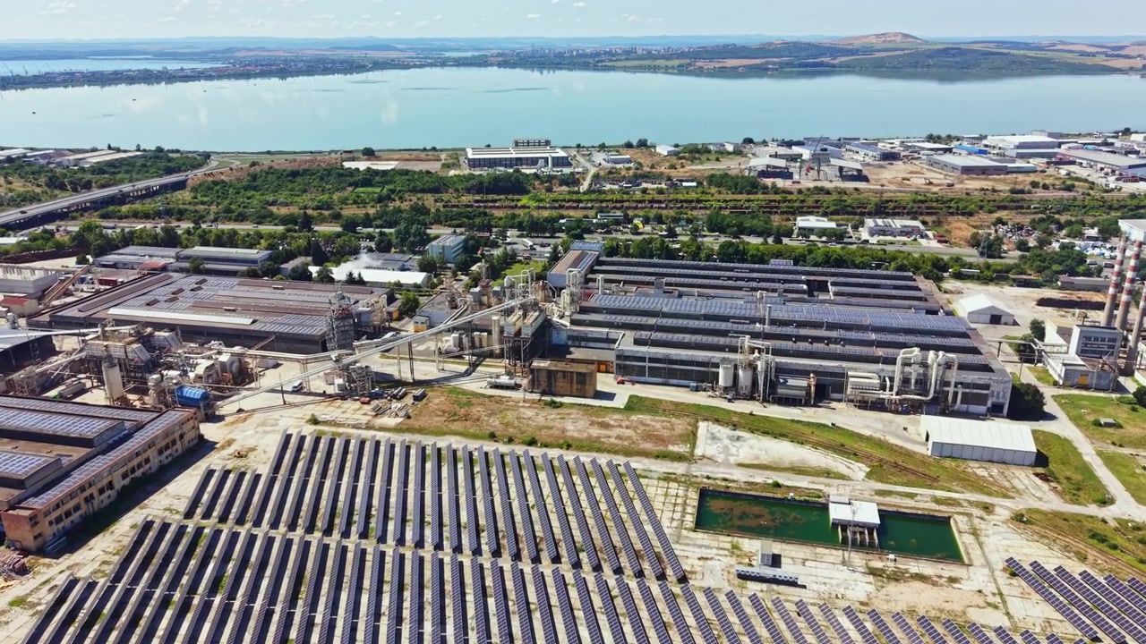 Pannelli solari coprono una vasta area vicino a un sito industriale in prossimità di uno specchio d'acqua in una giornata di sole