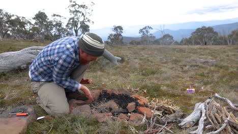 a man blows on a tinder buddle to get a fire going in the australian mountains