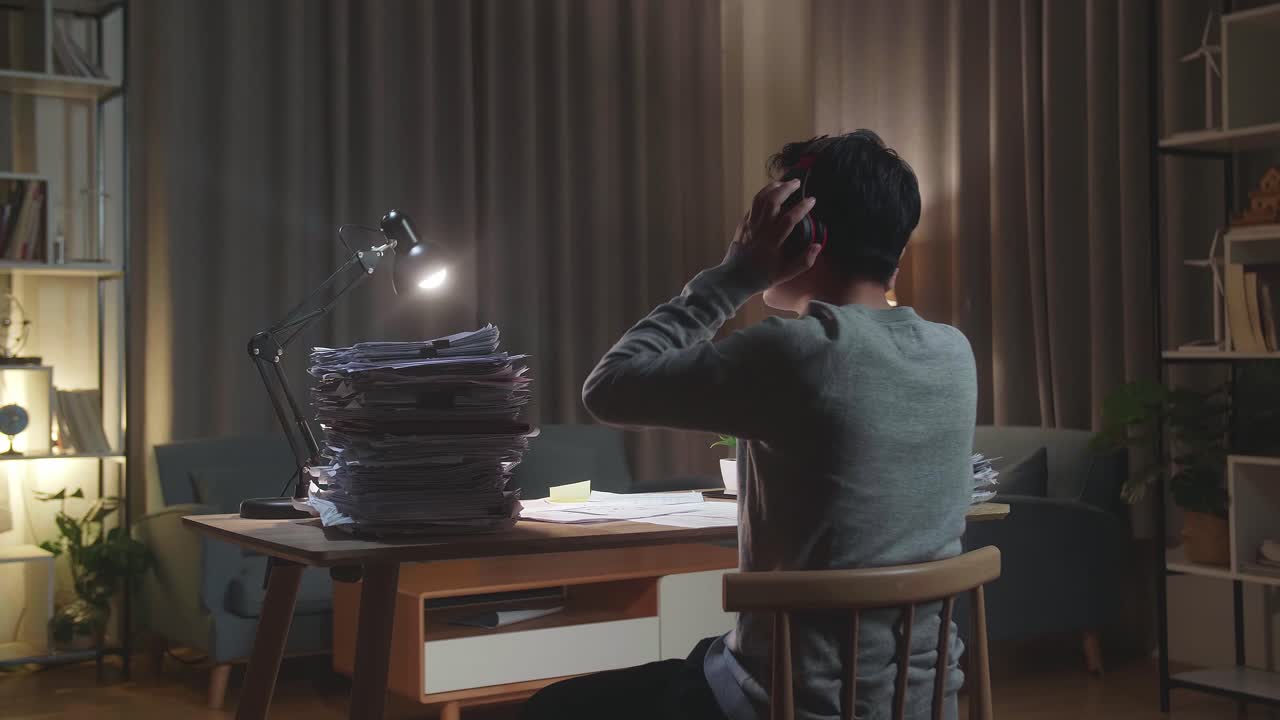 집 에서 문서 를 작업 한 후 에 헤드폰 을 착용 하고 음악 을 듣고 있는 아시아인 의 뒷면