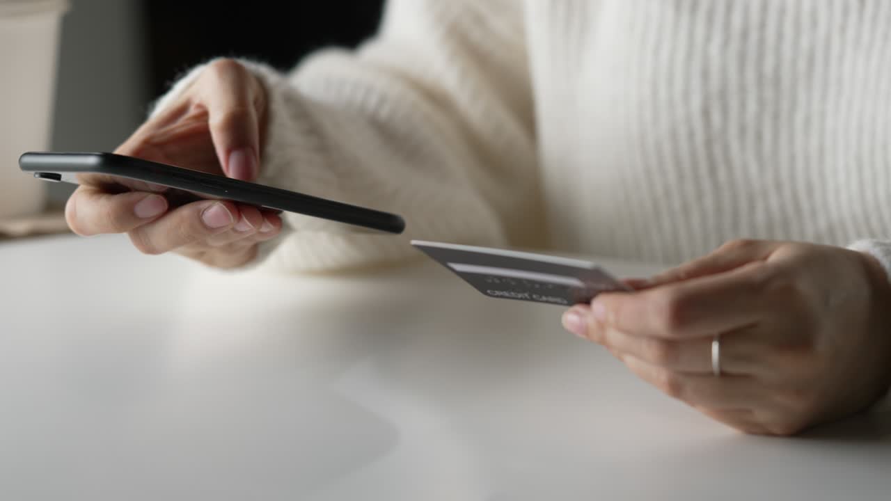 Mani femminili che tengono una carta di credito e usano uno smartphone. Acquisti online.