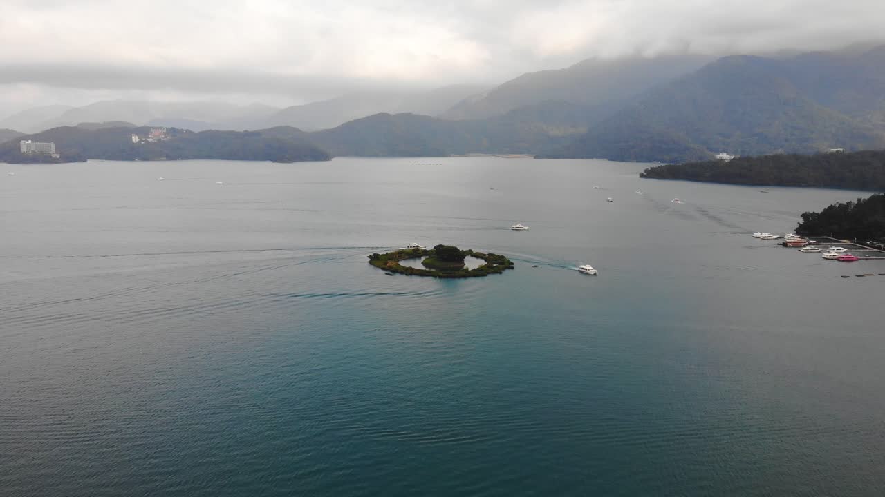 Sun Moon Lake in 4K drone aerial shot, fly over Lalu Island to the surrounding forest trees with a view of boats on Shuishe Pier, Yuchi Township, Nantou County, Taiwan.