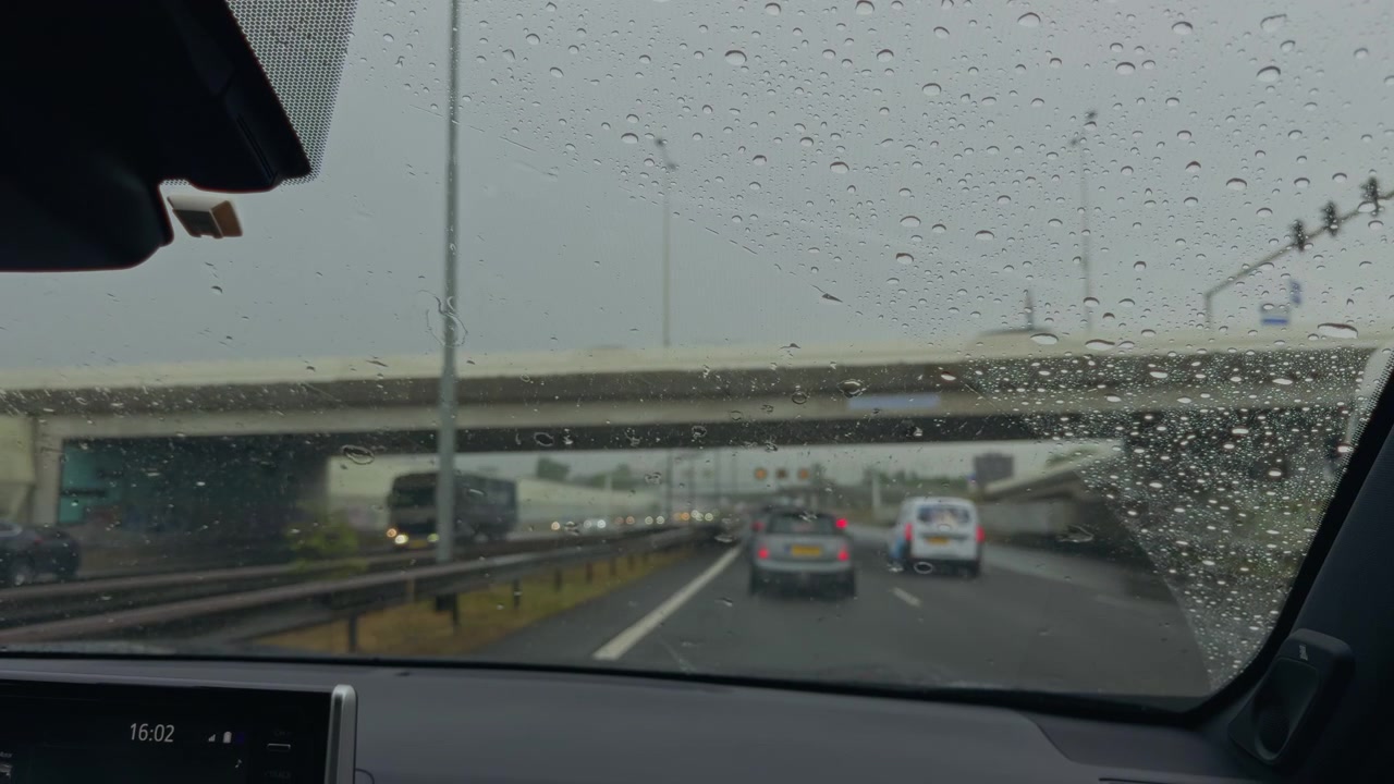 Passenger view from a moving car on a rainy highway with windscreen wipers clearing raindrops from the glass and traffic with head and tail lights and traveling in both lanes.