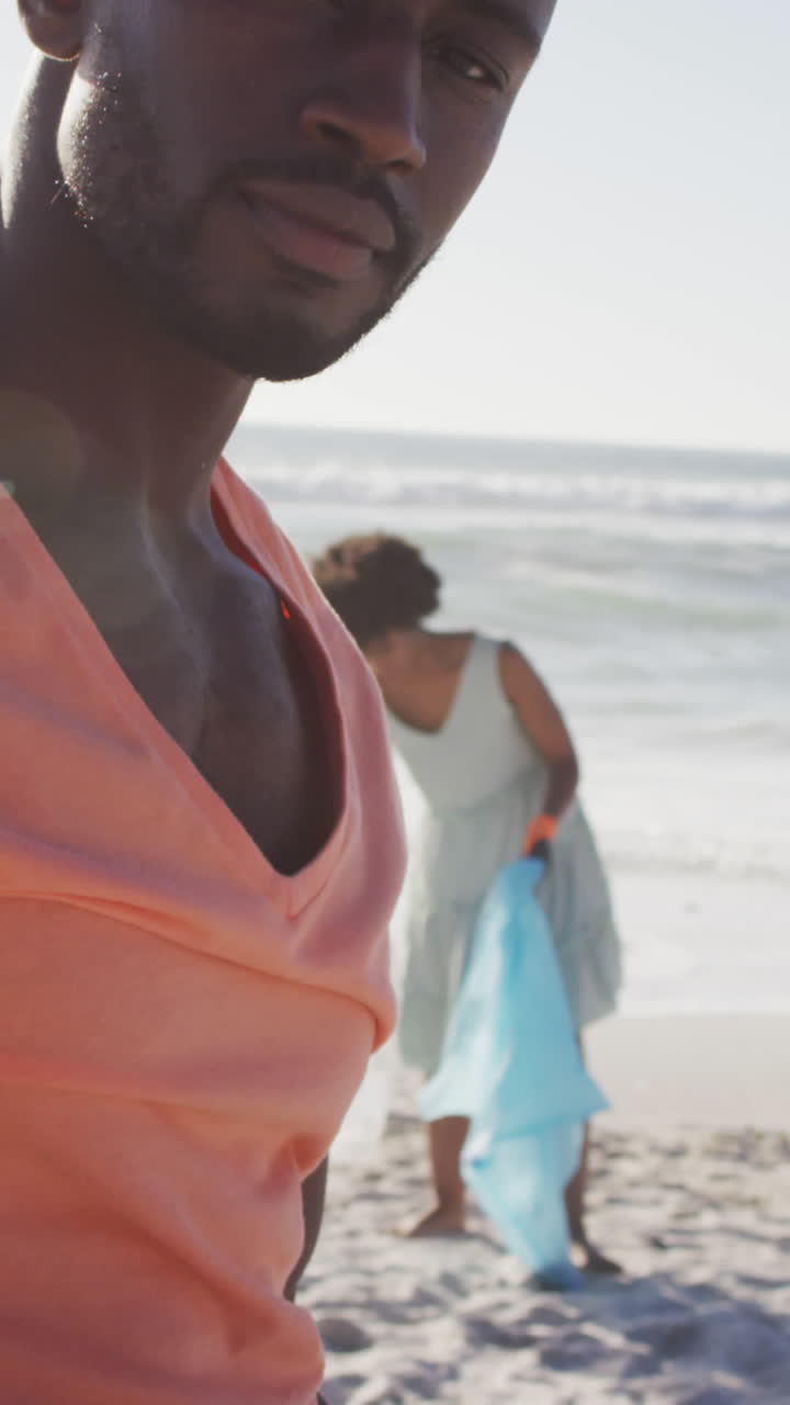 Portrait of african american couple segregating waste with gloves on sunny beach