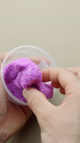hands playing with purple foam slime in transparent container, vertical