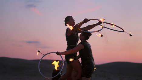 Mujeres-Con-Fuego-Al-Atardecer-En-La-Arena-Bailan-Y-Muestran-Trucos-Contra-El-Hermoso-Cielo-En-Cámara-Lenta