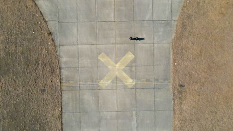 Aerial-drone-footage-looking-straight-down-of-people-walking-into-shot-from-top,-people-walking-on-old-disused-airfield