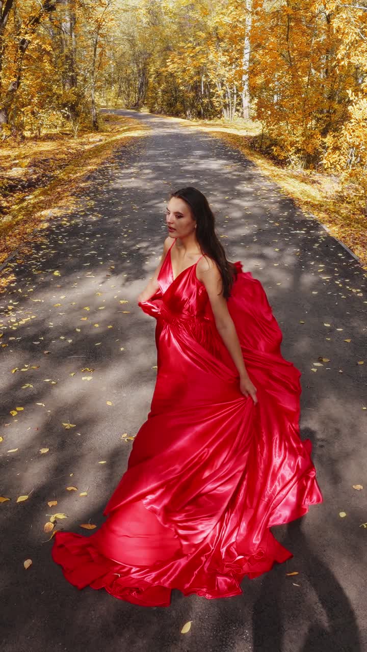 Un viaggio elegante: una donna con un fluente abito rosso cammina elegantemente lungo un sentiero autunnale ornato di foglie dorate e natura serena