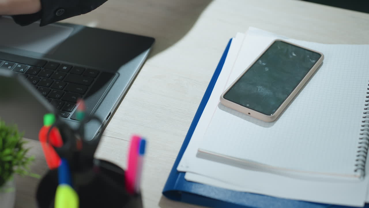 Close up of office worker placing folder with smartphone on desk, then adjusting laptop forward and preparing to open it in tidy workspace with bright lighting and organized accessories